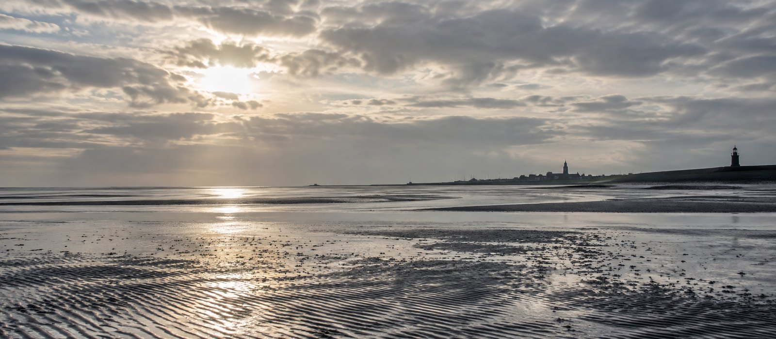 Waddenlicht over nat zand en een verre dijk, zilver bewolkt, zonder mensen